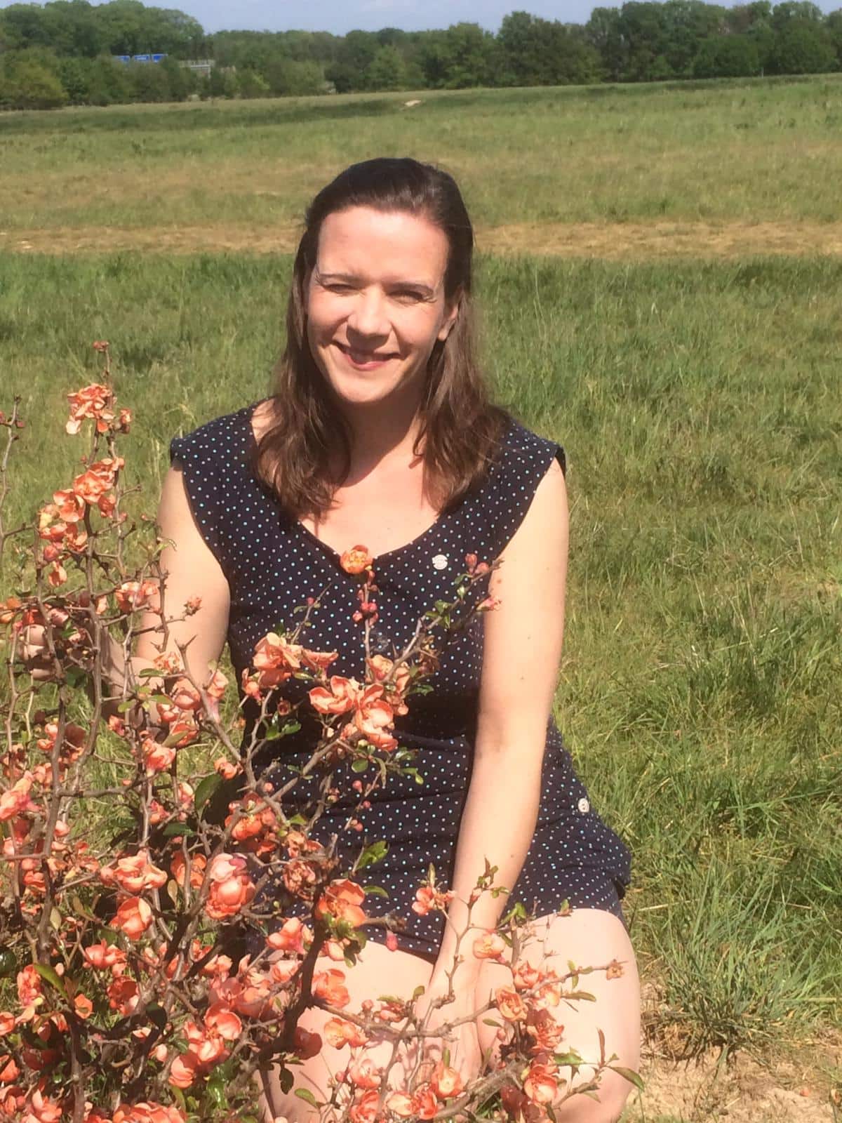 Britta Iven sitzt im Gras hinter einer blühenden Zierquitte und schaut lächelnd in die Kamera
